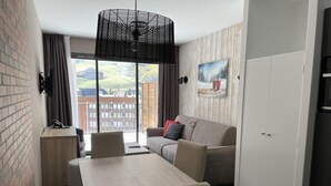 Ett hotellrum med ett matbord, stolar, en soffa, ett stort fönster och en tavla på väggen.