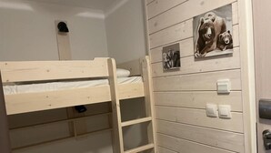 En våningssäng med en stege, en väggmonterad lampa och en dörr med en ljusknapp.