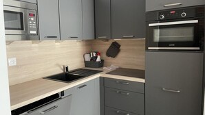 Una cocina compacta con armarios grises, microondas, horno empotrado y lavavajillas.