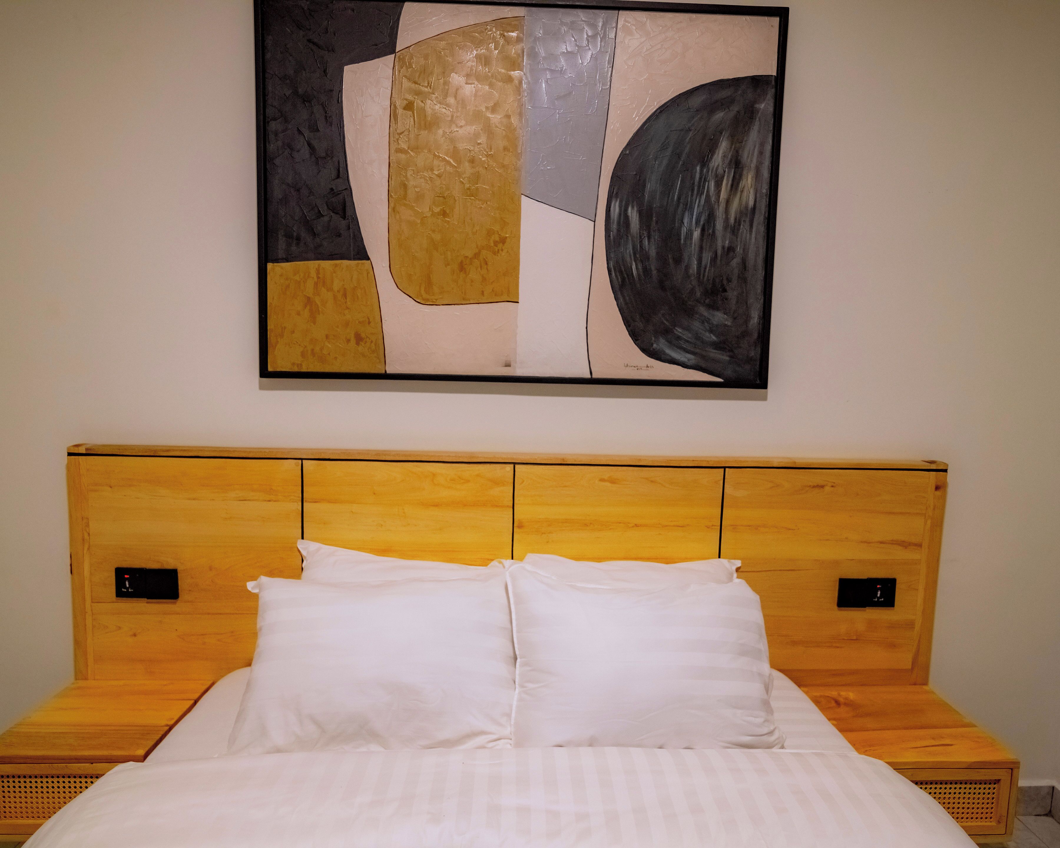 Una habitación de hotel con cabecera de madera, un cuadro abstracto grande en la pared y una cama bien hecha con sábanas blancas.
