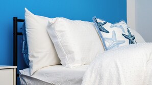 Een bed met witte lakens en blauwe kussens met een sterrenpatroon, tegen een blauwe muur.