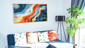 Een moderne woonkamer met een bank, kleurrijke kussens, een groot abstract schilderij, een vloerlamp en een potplant.