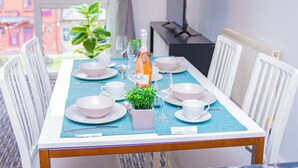 Een eettafel gedekt met witte borden, kommen en bestek, een klein plantje en een fles water.