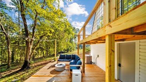 Une terrasse en bois avec un canapé et un espace salon, entourée d’arbres.