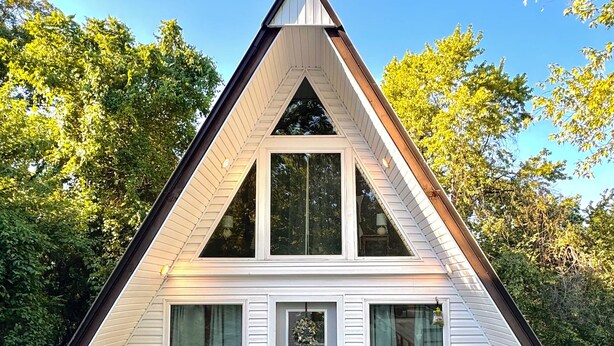 Un bâtiment de forme triangulaire, doté d’une porte centrale et de fenêtres, entouré d’arbres.
