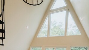 Un salon spacieux avec un plafond haut, de grandes fenêtres, un canapé moderne, une table basse en bois et un téléviseur à écran plat.