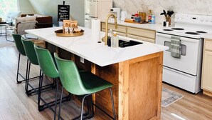 Une cuisine moderne dotée d’un îlot central, de tabourets de bar verts, d’un plan de travail blanc et d’un pare-feu en marbre.