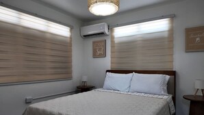 Une chambre à coucher comprenant un lit, deux tables de chevet, un climatiseur fixé au mur et un luminaire au plafond.