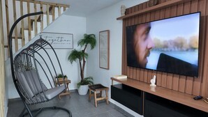 Un salon moderne avec un téléviseur, un fauteuil suspendu, une plante en pot et un escalier en bois.