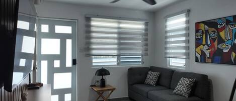 A modern living room with a dark grey sofa, a small wooden side table with a lamp, and a ceiling fan.