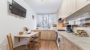 Une cuisine moderne avec des meubles en bois, un four encastré, une machine à café et un coin repas comprenant une table et des chaises.