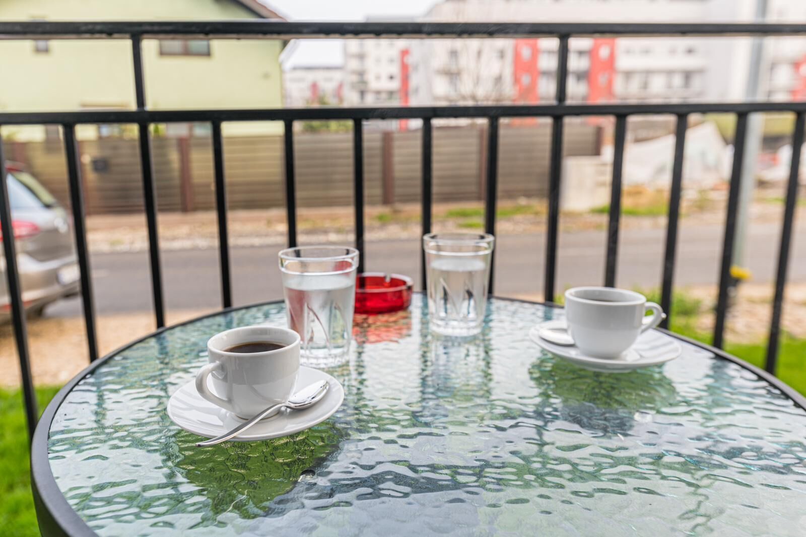 A round glass table with two white cups and a glass of water, a red candle, and a metal spoon.