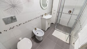 Une salle de bain moderne comprenant des toilettes, un bidet, un lavabo et une douche séparée par une paroi en verre.
