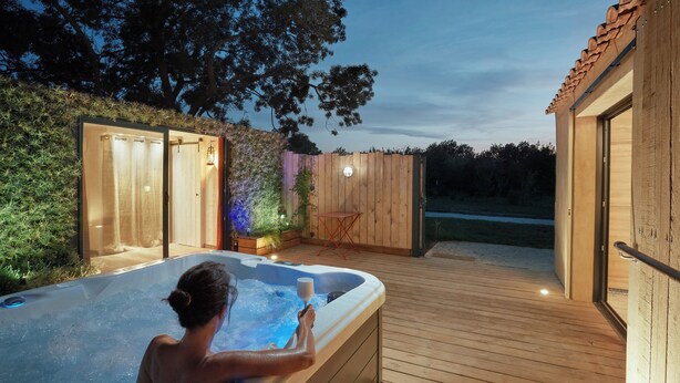 A hot tub on a wooden deck with a wooden fence and a small table. - Pine Lodge and Spa (La Garde)