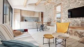 A modern living room with a stone wall, a flat-screen TV, a sofa, and a dining area with stools. - Pine Lodge and Spa (La Garde)