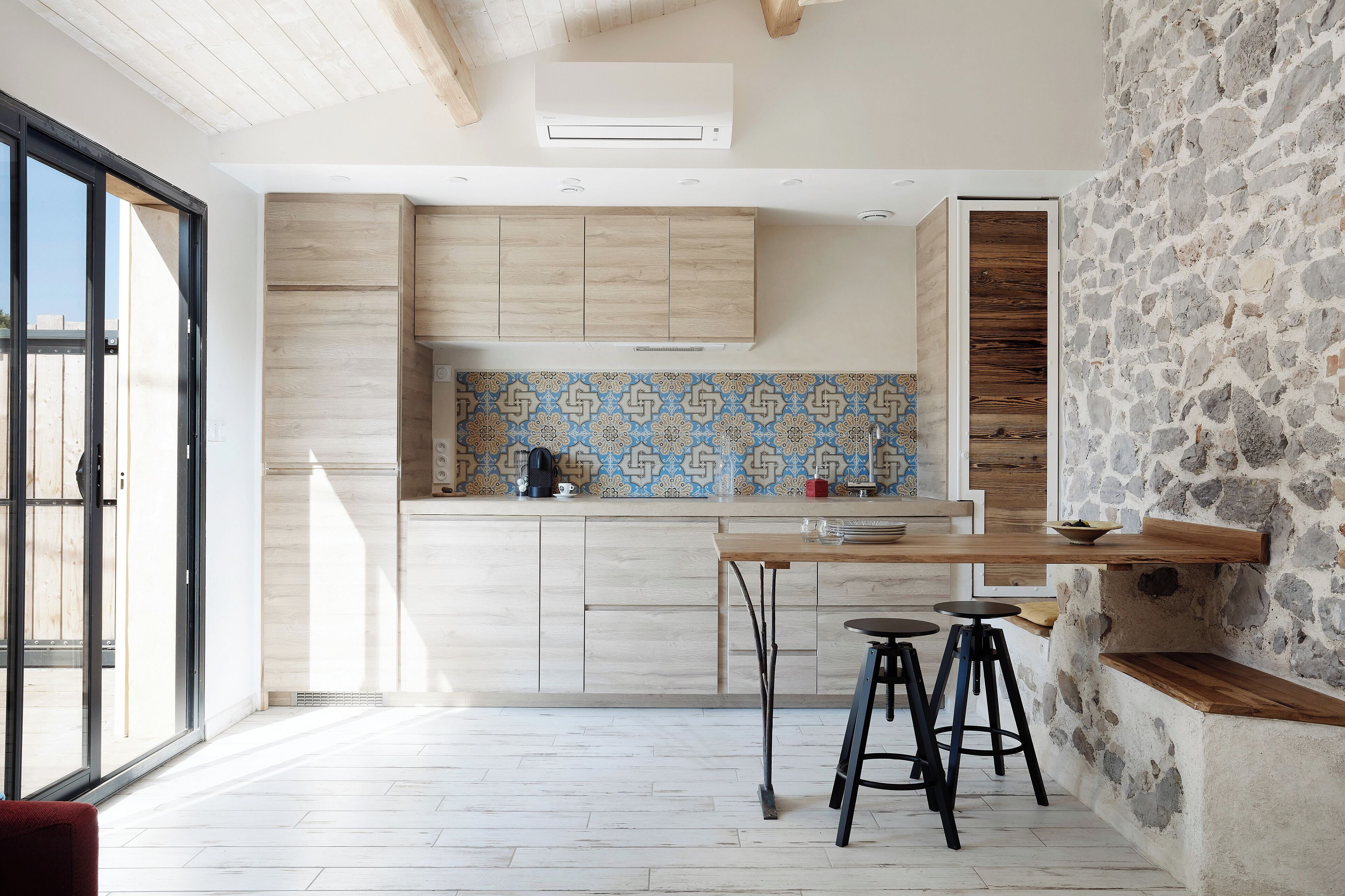 Une cuisine moderne avec des armoires en bois, un dosseret à motifs et un mur d’accent en pierre.