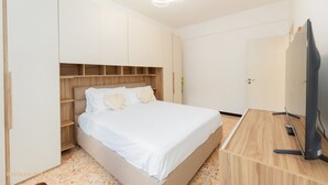 A bedroom with a bed, wooden headboard, built-in shelving, a TV, and a door. - Rapallo Vintage House (Rapallo)