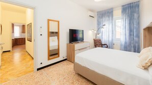 Hotelkamer met een bed, een televisie, een bureau en een stoel. Er is een deur die naar een andere kamer leidt.