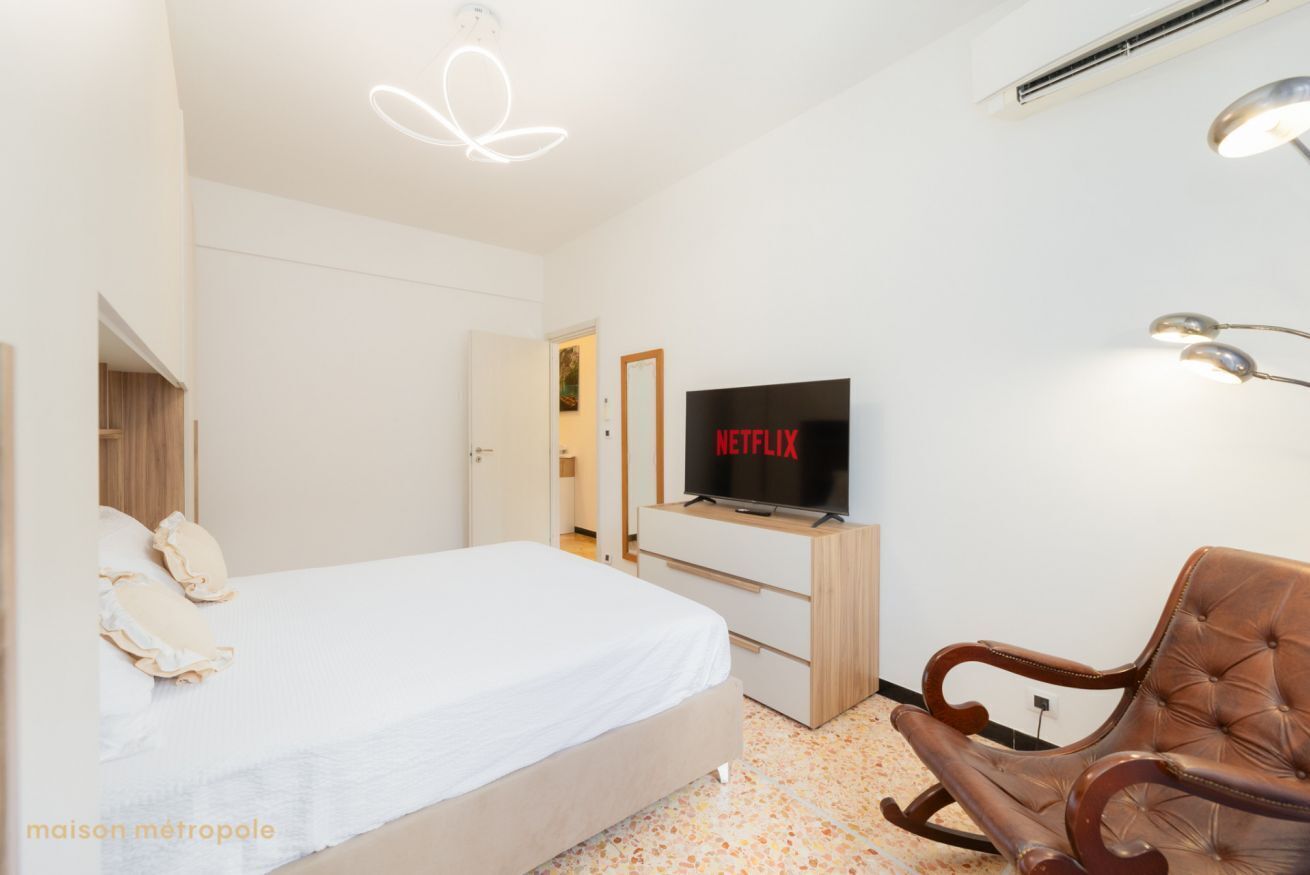 Moderni hotellihuone, jossa on sänky, televisio, puinen tuoli ja ainutlaatuinen kattovalaisin.