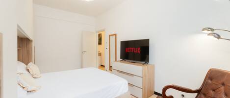 Moderni hotellihuone, jossa on sänky, televisio, puinen tuoli ja ainutlaatuinen kattovalaisin.
