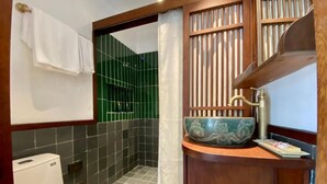 Une salle de bain comprenant des toilettes, un lavabo agrémenté d’un récipient décoratif et un espace douche aux carreaux verts.