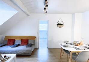 Sala de estar moderna com sofá, mesa de jantar e vista para o mar através de uma porta.