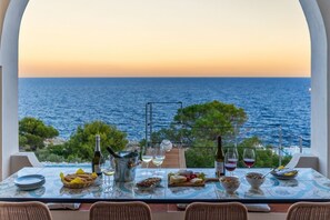 A table set for a meal with a view of the sea at sunset.