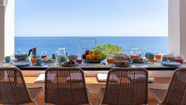 A breakfast table with a view of the sea, wicker chairs, and a variety of breakfast items. - Villa Horama - Waterfront with Infinity Pool (Siracusa)