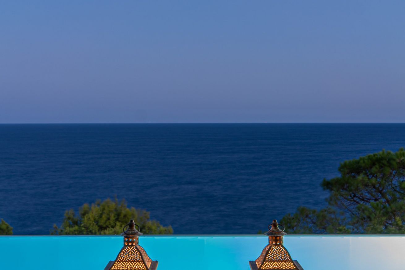 A poolside view with a clear view of the sea and a white wall.