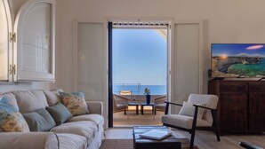 A living room with a sofa, armchairs, a coffee table, and a TV. There is a balcony with a view of the sea. - Villa Horama - Waterfront with Infinity Pool (Siracusa)