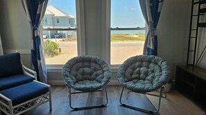 A room with two cushioned chairs, a blue sofa, and a large window with a view of a house and beach.