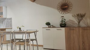 A dining area with a wooden table and chairs, a white cabinet, and decorative items including a flower arrangement and a vase with reeds. - MAISONETTE PROVENCALE (Le Thor)