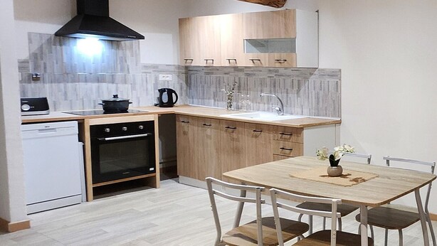 A compact kitchen with wooden cabinets, a built-in oven, a black range hood, and a small dining table with chairs. - MAISONETTE PROVENCALE (Le Thor)