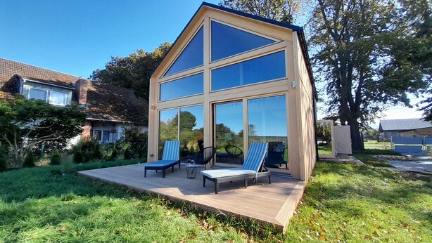 A modern house with a large glass facade, a wooden deck, and two lounge chairs. - Villa Leone - spacious, breathtaking in harmony with nature (Nowe Warpno)
