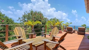 Une terrasse en bois avec des meubles d’extérieur, des plantes en pot et une vue sur l’océan.