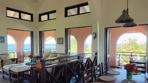 Une salle à manger spacieuse, dotée de hauts plafonds et de grandes fenêtres, offrant une vue sur l’océan.