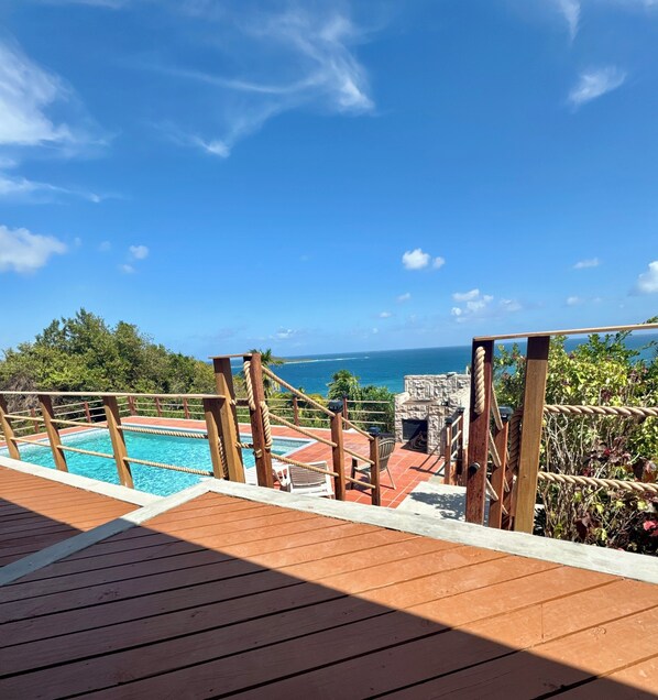A wooden deck with a pool, a stone fireplace, and a view of the ocean.