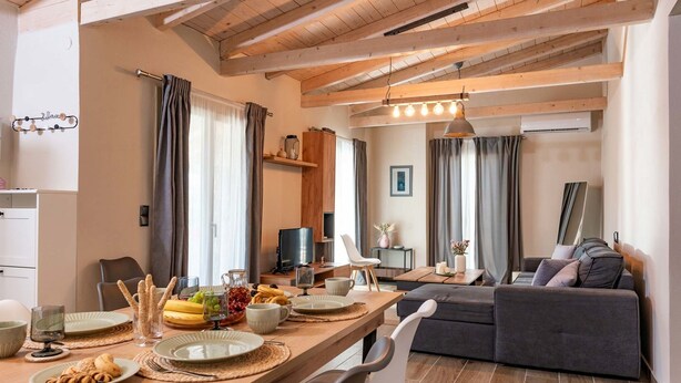 Ein modernes Wohnzimmer mit einer Couch, einem Esstisch gedeckt mit Tellern und Gläsern sowie einem Fernseher.