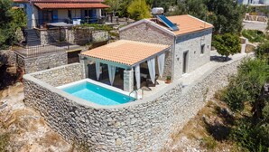 Une piscine bordée de pierres, avec un patio couvert, entourée de murs de pierre et de végétation.