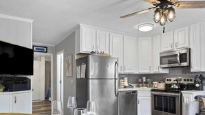 A modern kitchen with white cabinets, stainless steel appliances, a dining table set with plates and glasses, and a ceiling fan. - Classic Coastal Condo, Oceanview, Short Walk to Coligny, & Free New Bikes! (Hilton Head Island)