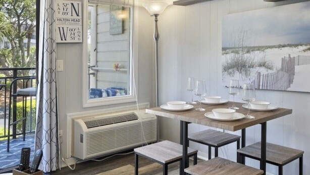 A dining area with a table set for four, a standing lamp, and a large painting on the wall. - Classic Coastal Condo, Oceanview, Short Walk to Coligny, & Free New Bikes! (Hilton Head Island)