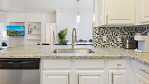 Una cucina moderna con mobili bianchi, un piano di lavoro in granito, un lavello in acciaio inossidabile e una parete di fondo rivestita con piastrelle bianche e nere.