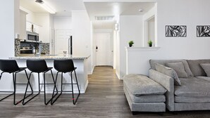 Una cucina moderna con isola centrale, sgabelli da bar, un divano grigio e opere d'arte astratte alle pareti.