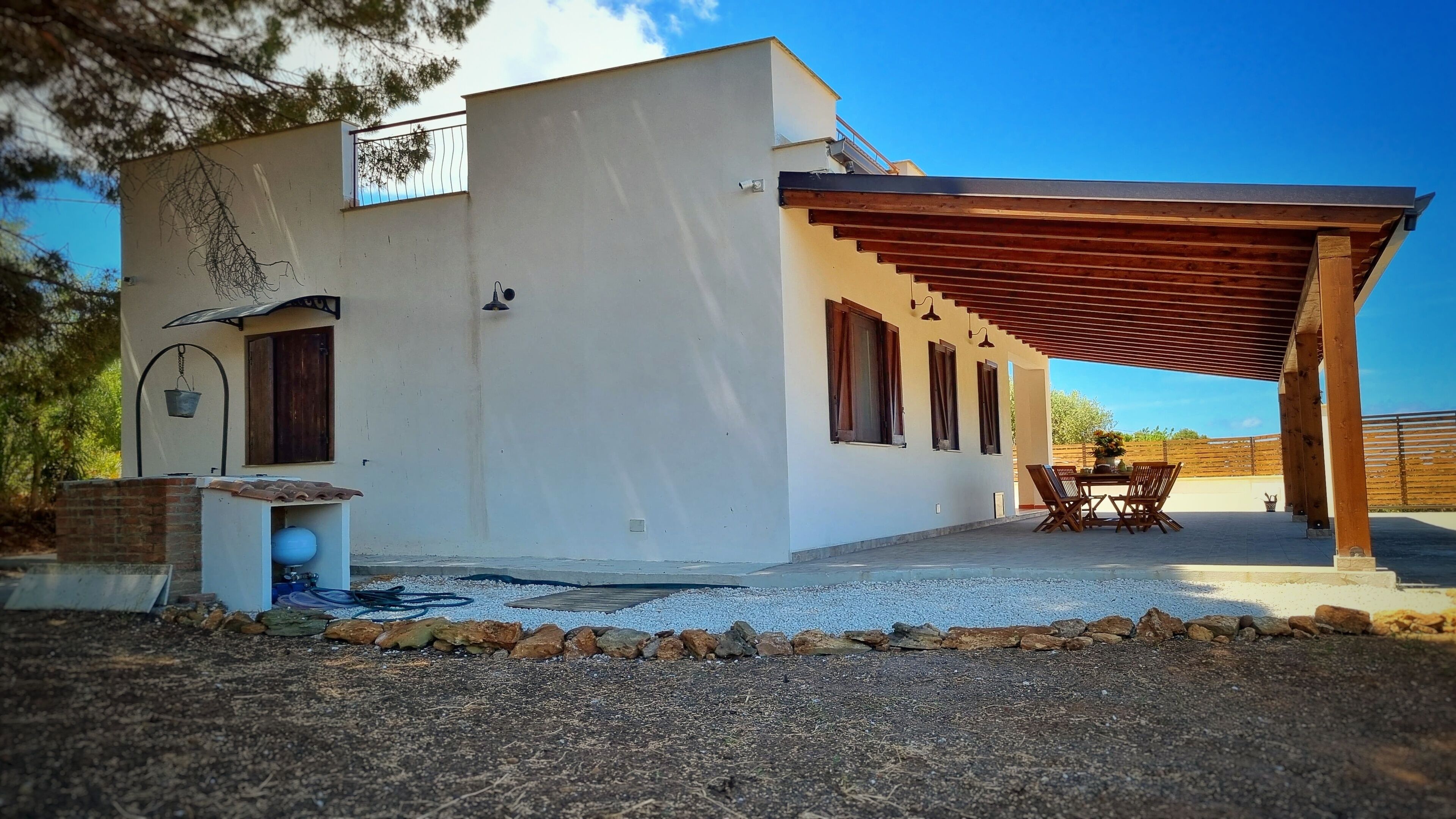 Una casa moderna con patio coperto, angolo cottura esterno e vialetto in ghiaia.
