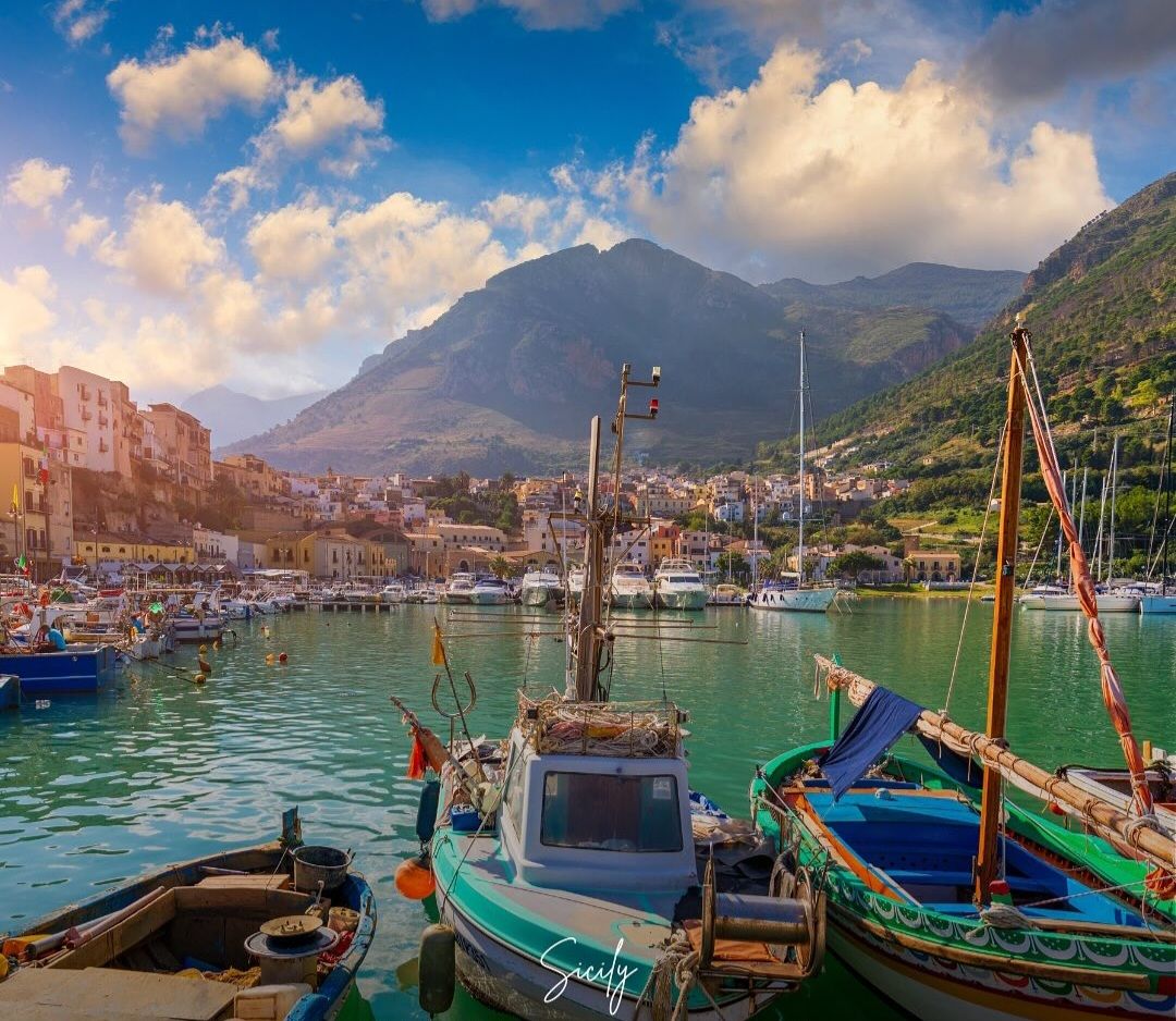 Un puerto con barcos amarrados, montañas al fondo y edificios a lo largo del paseo marítimo.