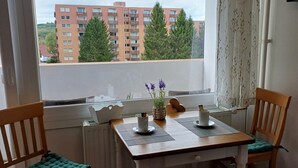 A dining area with a table and chairs, a view of a building, and a window with curtains. - "Waldgeflüster" apartment with Harz romance. (Altenau)