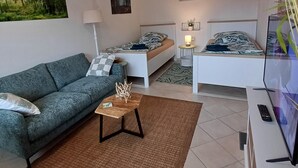 A modern living room with a sofa, a coffee table, a bed, and a TV. - "Waldgeflüster" apartment with Harz romance. (Altenau)