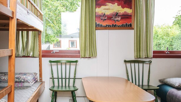 A room with a bunk bed, two chairs, a table, and a painting of boats on the wall. - 4 Person Holiday Park Home in Grindsted (Grindsted)