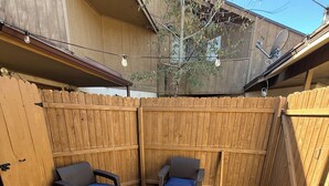 Una terraza de madera con dos sillas de mimbre y un banco, rodeada por una valla de madera.