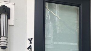 Eine schwarze Tür mit Milchglasscheibe, einem Zahlenschloss und einer kleinen Außenleuchte darüber.